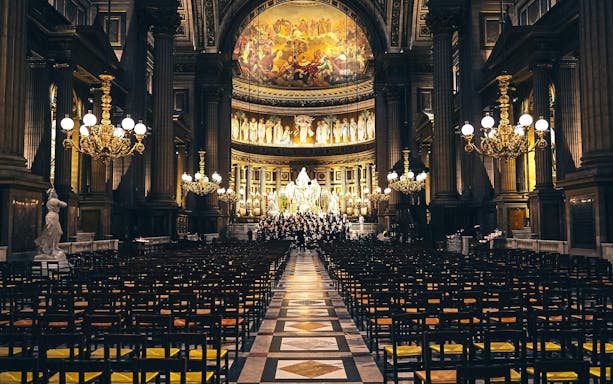 Orchestra performing in The Church of St Madeleine, Paris, France, with ornate interior and chandeliers.