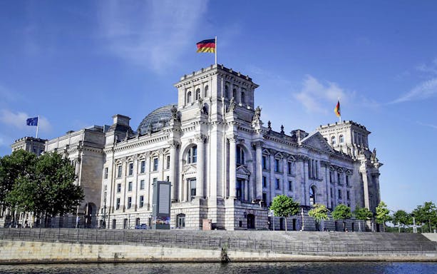 Reichstag building in Berlin with glass dome and tourists on rooftop terrace.