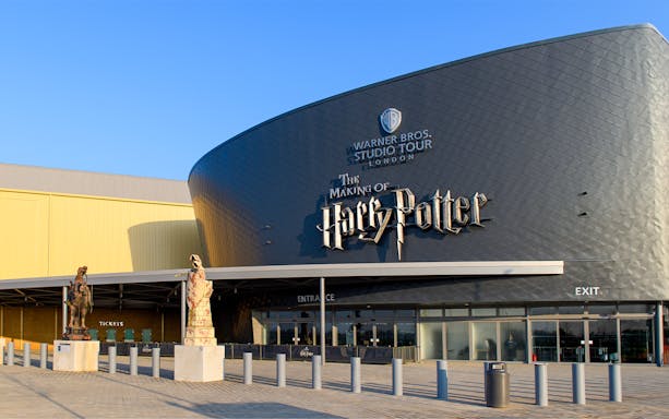 Warner Bros. Studio Tour London entrance with Harry Potter-themed statues and visitors.