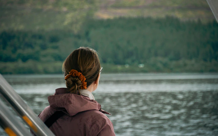 Person on a boat looking at Loch Ness with forested hills in the background.