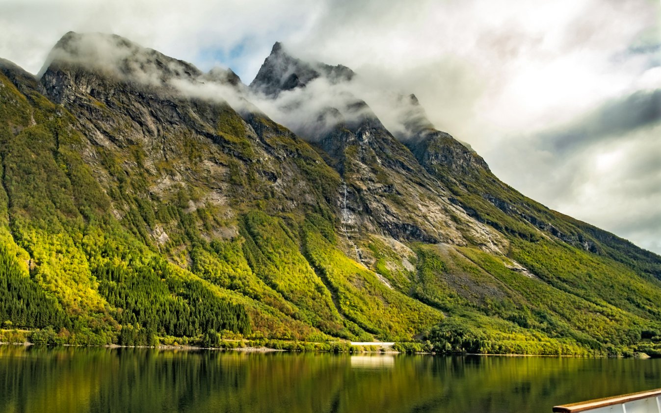 Landscape of Hjørundfjord, Norway with misty mountains and reflective water.