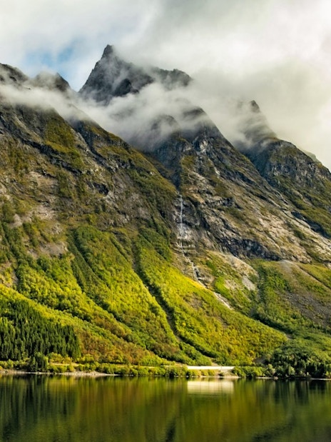 Landscape of Hjørundfjord, Norway with misty mountains and reflective water.