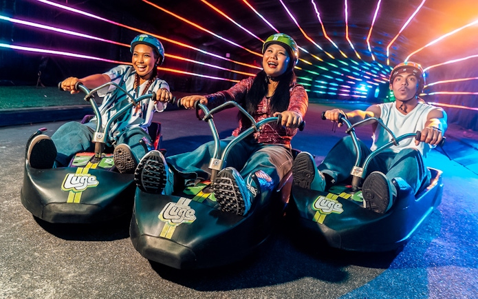 Friends enjoying night luge ride under colorful lights in Singapore.