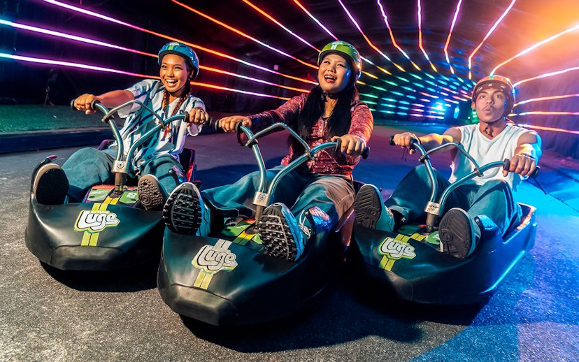 Friends enjoying night luge ride under colorful lights in Singapore.