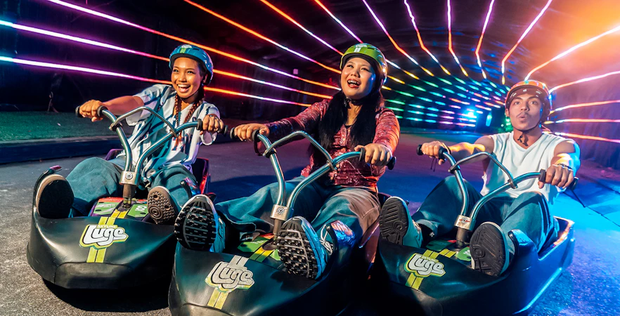 Friends enjoying night luge ride under colorful lights in Singapore.