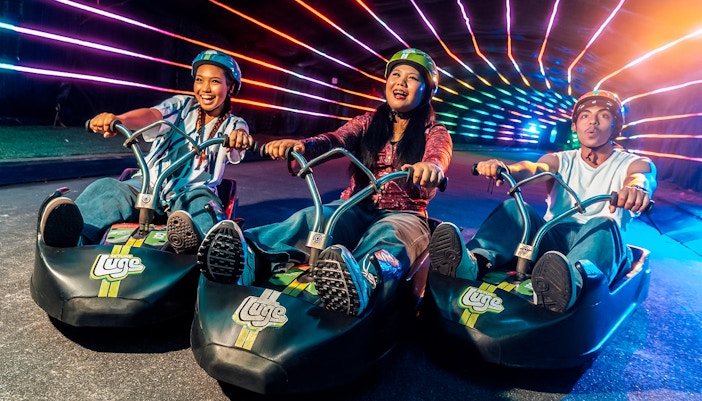 Friends enjoying night luge ride under colorful lights in Singapore.