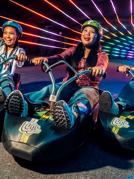 Friends enjoying night luge ride under colorful lights in Singapore.
