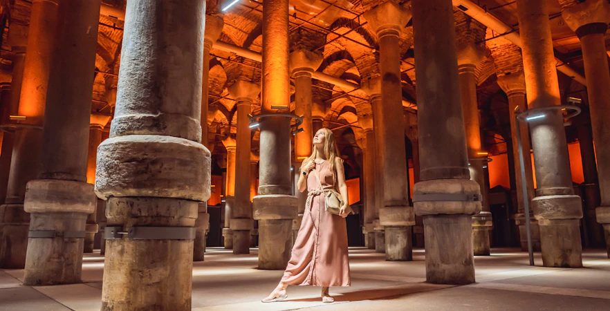Visitor exploring the illuminated columns of the Basilica Cistern in Istanbul.
