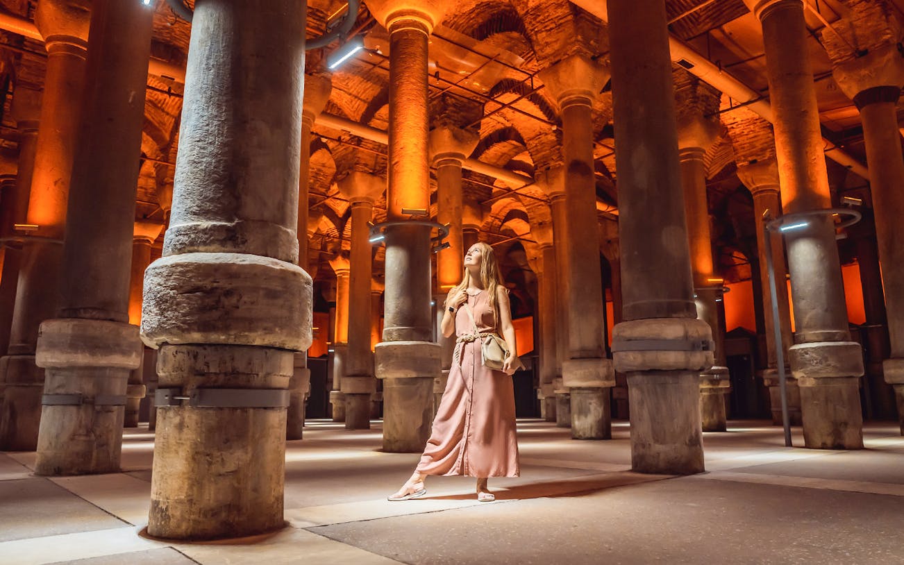 Visitor exploring the illuminated columns of the Basilica Cistern in Istanbul.