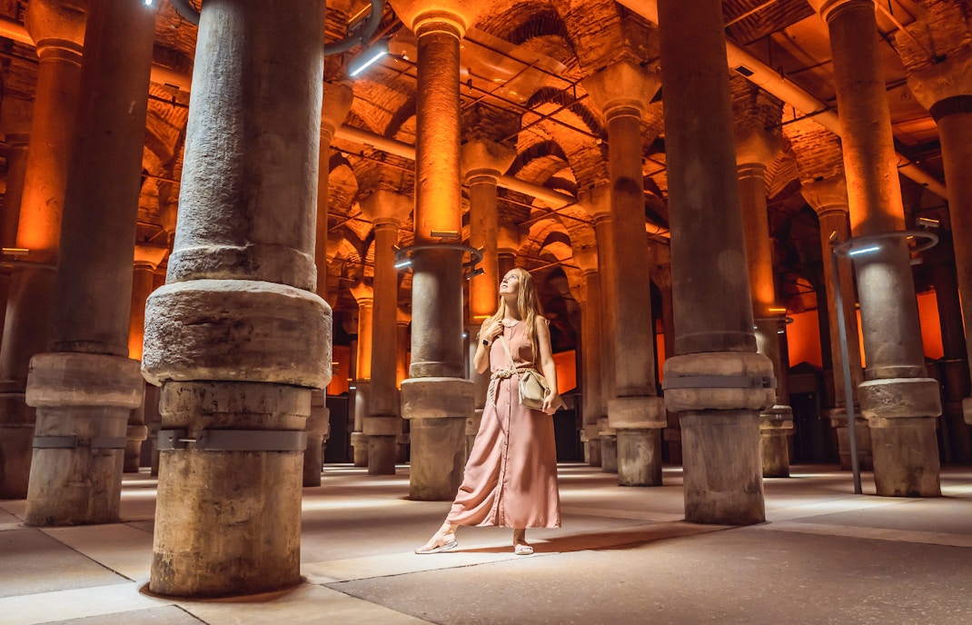 Woman exploring Basilica Cistern, Istanbul, with illuminated columns and arches.
