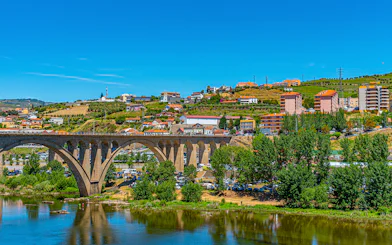 Bridge over Douro River with hillside vineyards and buildings in Peso da Régua, Portugal.
