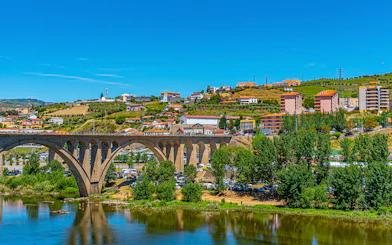 Bridge over Douro River with hillside vineyards and buildings in Peso da Régua, Portugal.