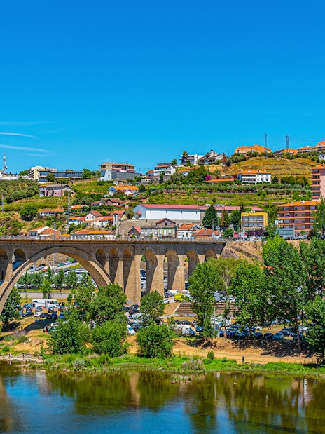 Bridge over Douro River with hillside vineyards and buildings in Peso da Régua, Portugal.
