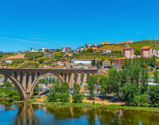 Bridge over Douro River with hillside vineyards and buildings in Peso da Régua, Portugal.