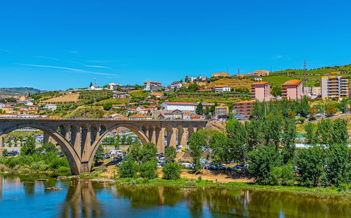 Bridge over Douro River with hillside vineyards and buildings in Peso da Régua, Portugal.