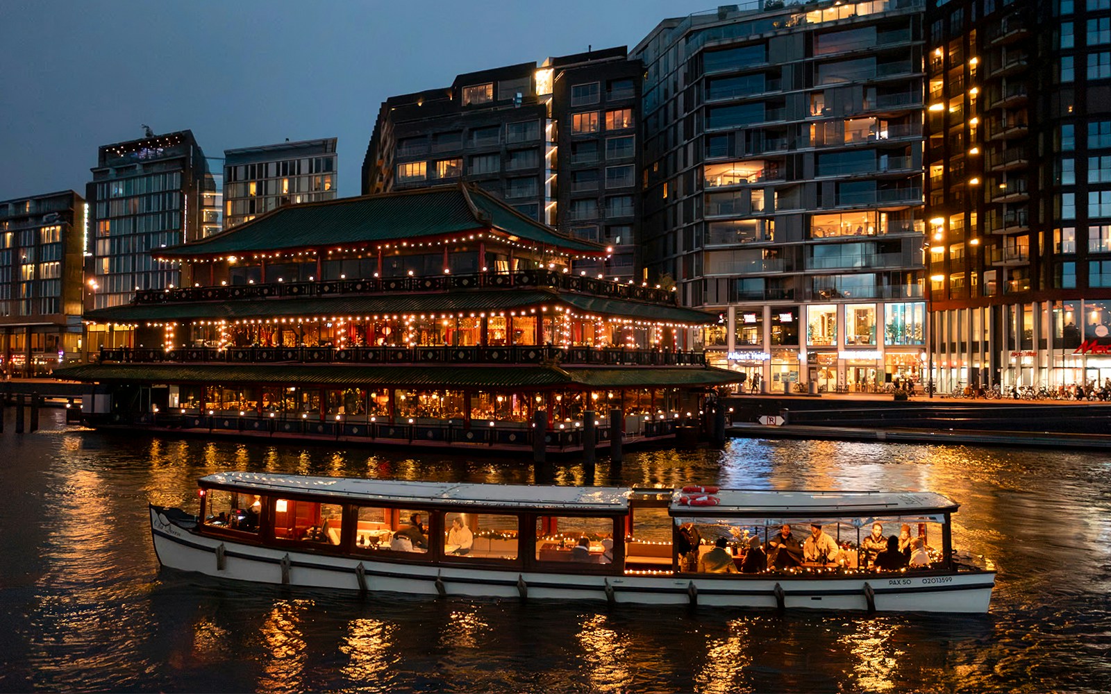 Cruise boat passing illuminated building during Amsterdam Light Festival.
