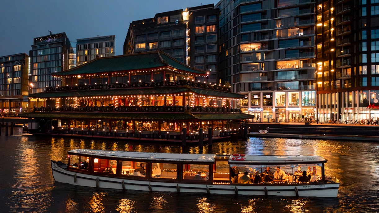 Cruise boat passing illuminated building during Amsterdam Light Festival.
