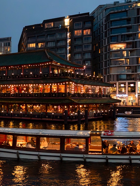 Cruise boat passing illuminated building during Amsterdam Light Festival.