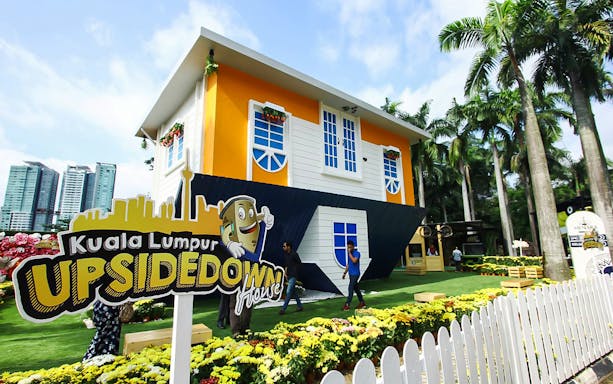 Kuala Lumpur Upside Down House with visitors and city skyline in the background.