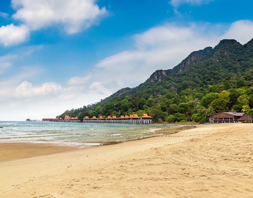 Tourists parasailing over Pantai Kok Beach, Langkawi, with lush green hills in the background.