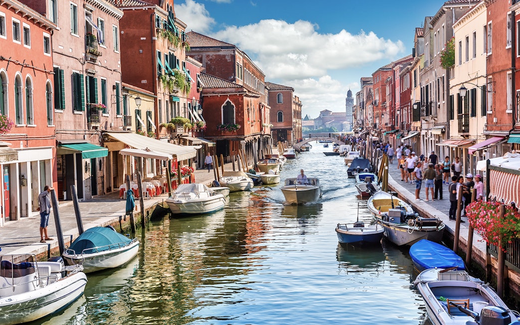 Venice canal with boats and colorful buildings, part of Venice City Pass attractions.