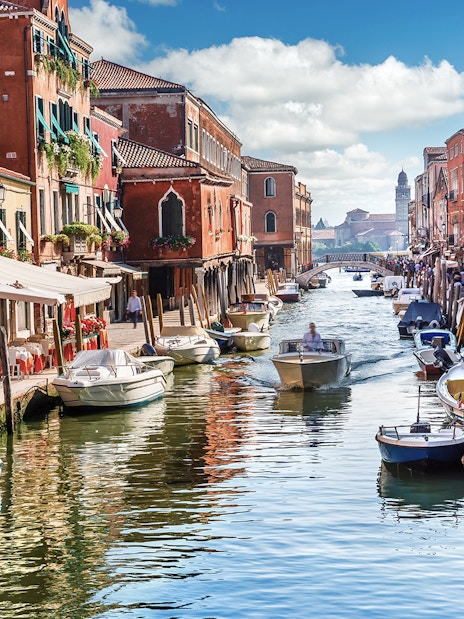 Venice canal with boats and colorful buildings, part of Venice City Pass attractions.