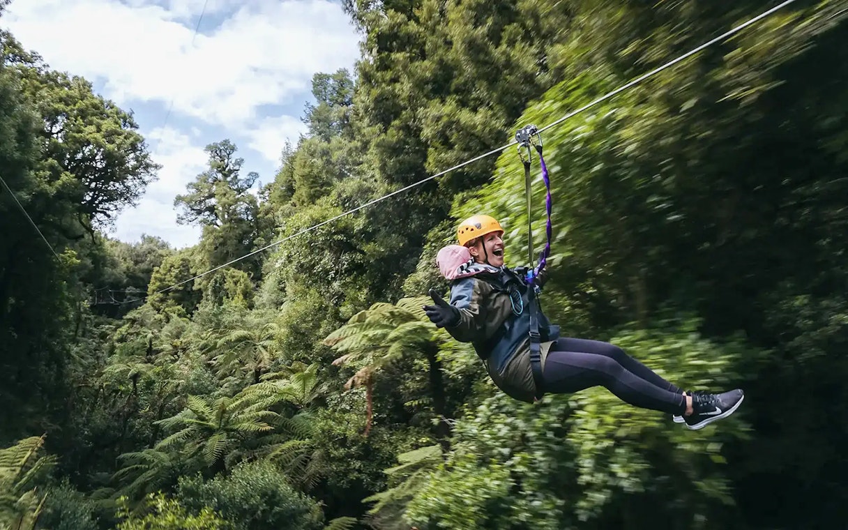 Person ziplining through lush Rotorua forest.