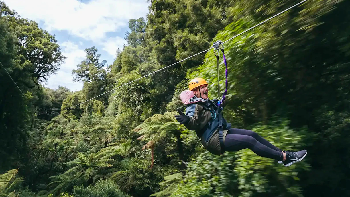 Person ziplining through lush Rotorua forest.