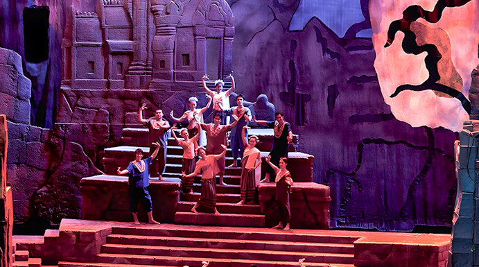Siam Niramit Phuket performers in traditional attire on stage with ancient temple backdrop.