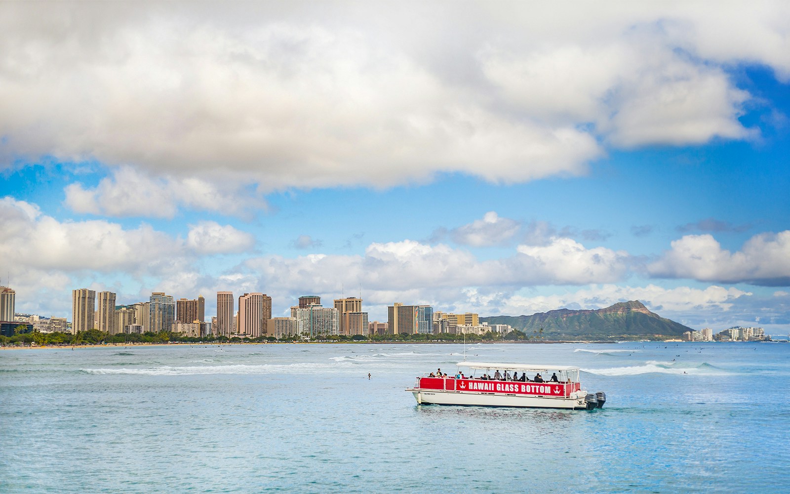 Glass-bottom boat on water with Honolulu skyline and Diamond Head in background.