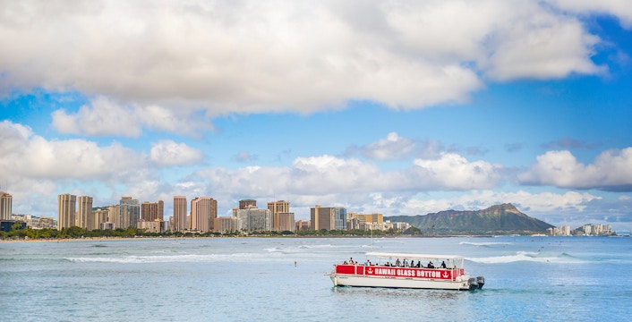 Glass-bottom boat on water with Honolulu skyline and Diamond Head in background.