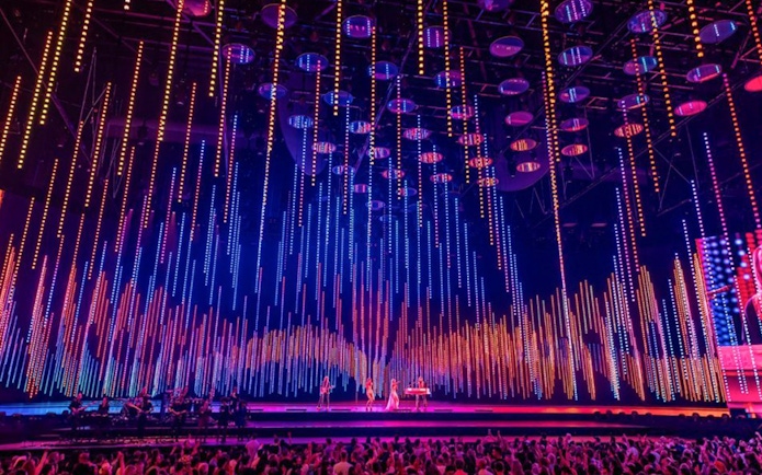 ABBA Voyage concert stage with colorful light display and audience.