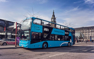 Hop-on hop-off bus in Hamburg city center near historic clock tower.