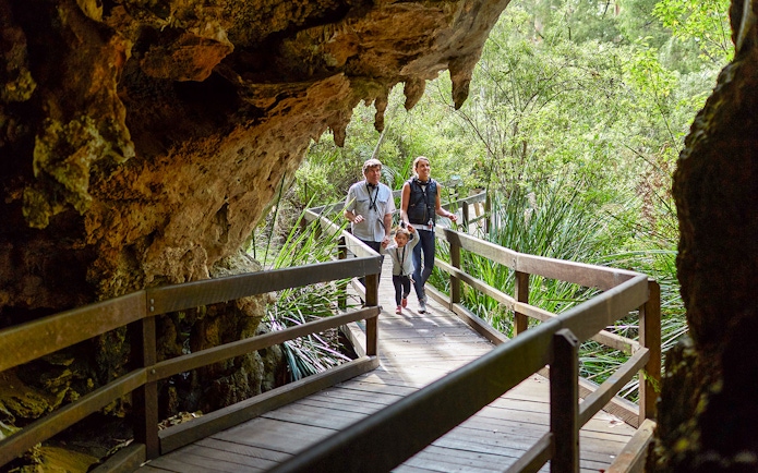 Family walking on a wooden path through Mammoth Cave, Margaret River, surrounded by lush greenery.