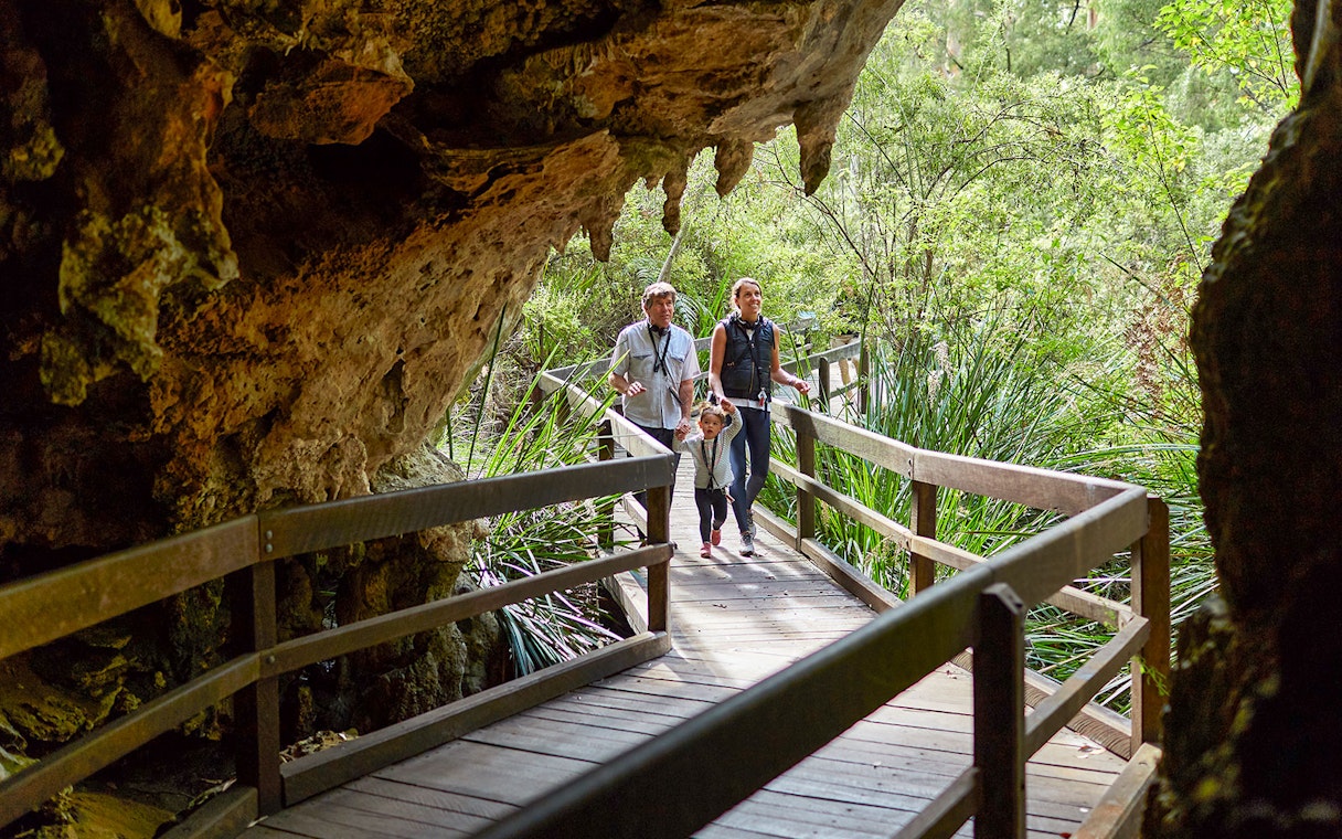 Family walking on a wooden path through Mammoth Cave, Margaret River, surrounded by lush greenery.