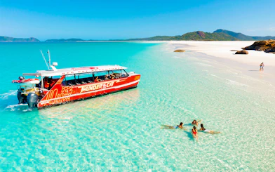 Thundercat boat near Whitsundays beach with people swimming in clear water.