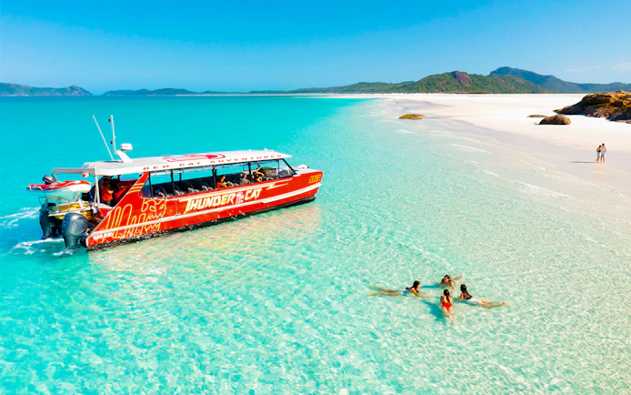 Thundercat boat near Whitsundays beach with people swimming in clear water.