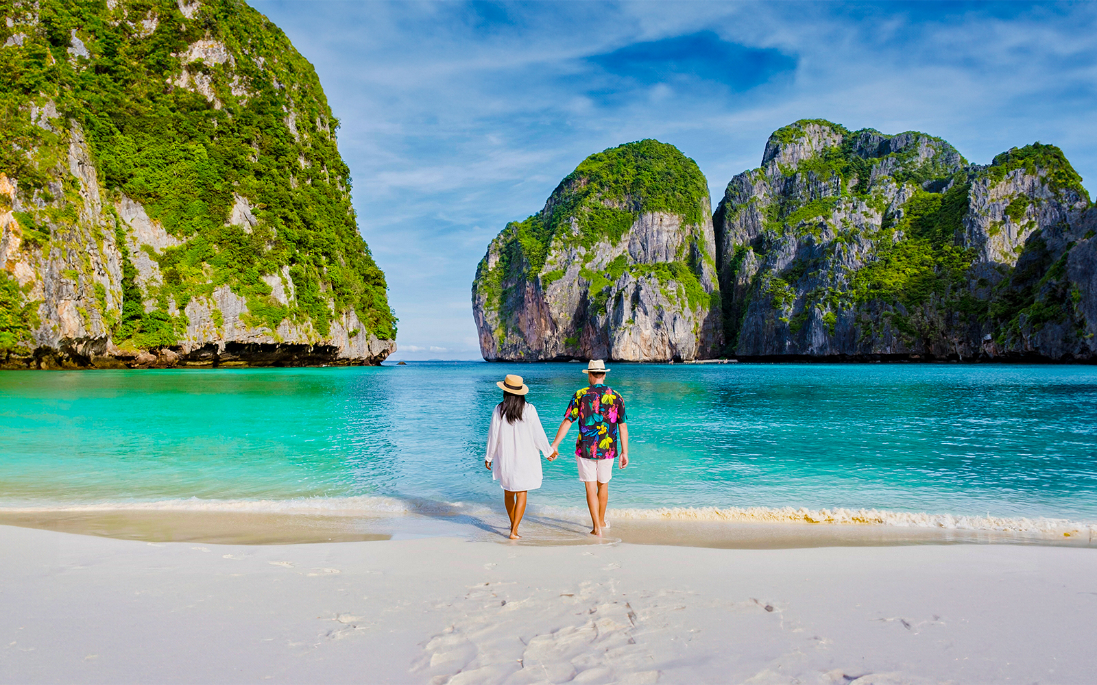 Couple walking on beach towards longtail boat in Koh Phi Phi lagoon, Thailand.