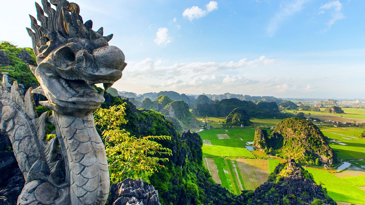 Panoramic view from Mua Caves viewpoint, Ninh Bình, Vietnam, with stone dragon sculpture in foreground.