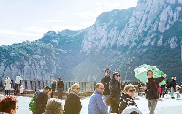 Tourists at Montserrat viewpoint with mountain backdrop, Spain.