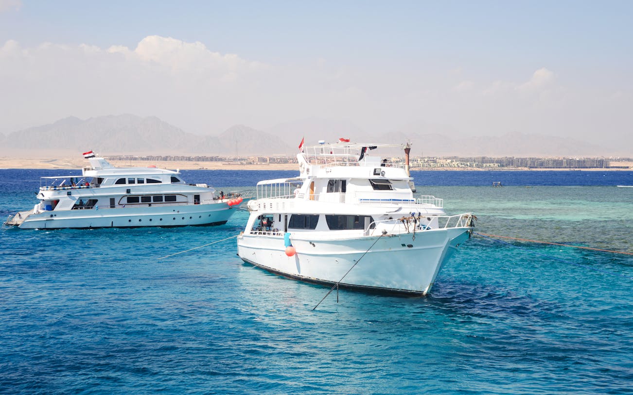 Tourists snorkeling in clear waters near Tiran Island, Sharm El Sheikh, with vibrant coral reefs visible.