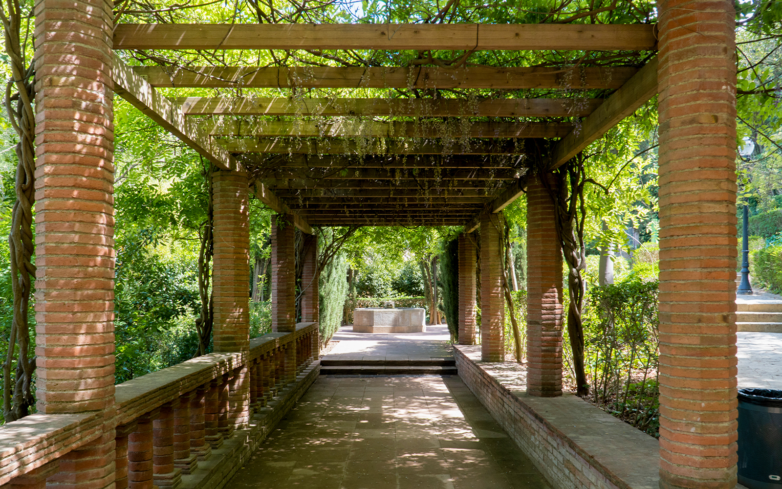 Pergola walkway in Laribal Garden, Barcelona, with brick columns and lush greenery.