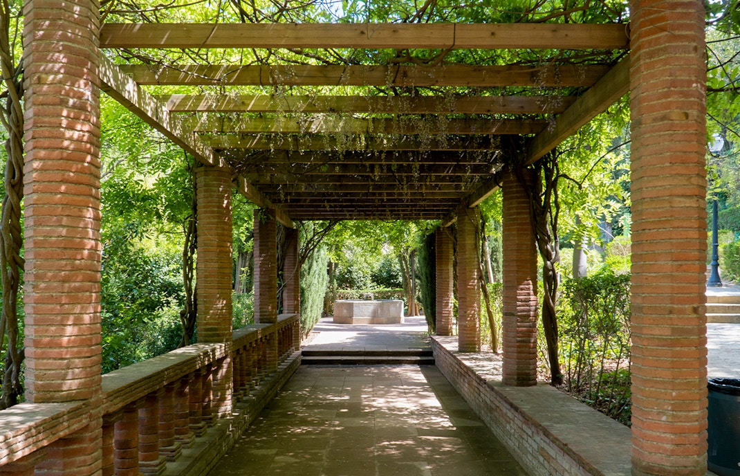Pergola walkway in Laribal Garden, Barcelona, with brick columns and lush greenery.