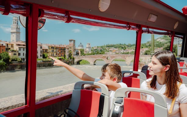 Hop-on hop-off bus tour in Verona with view of Ponte Pietra and cityscape.