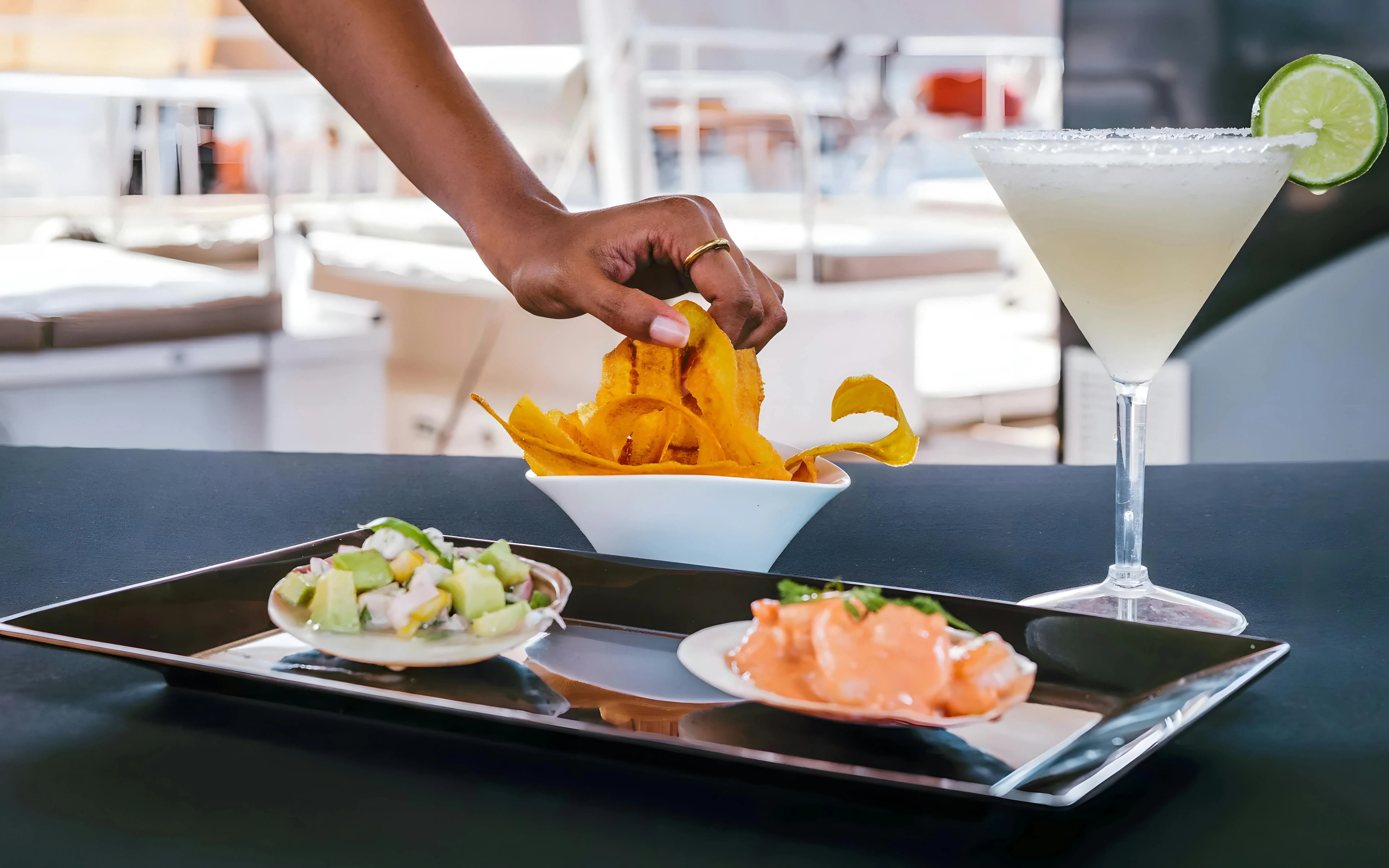 Hand reaching for plantain chips with ceviche and cocktail on Rosario Islands catamaran cruise.