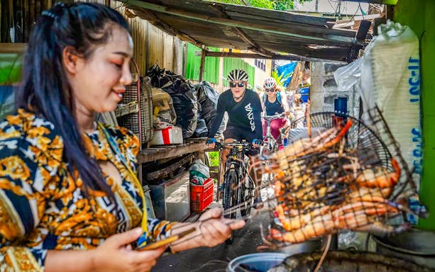 Cyclists on a guided tour pass a street food vendor in Bangkok.