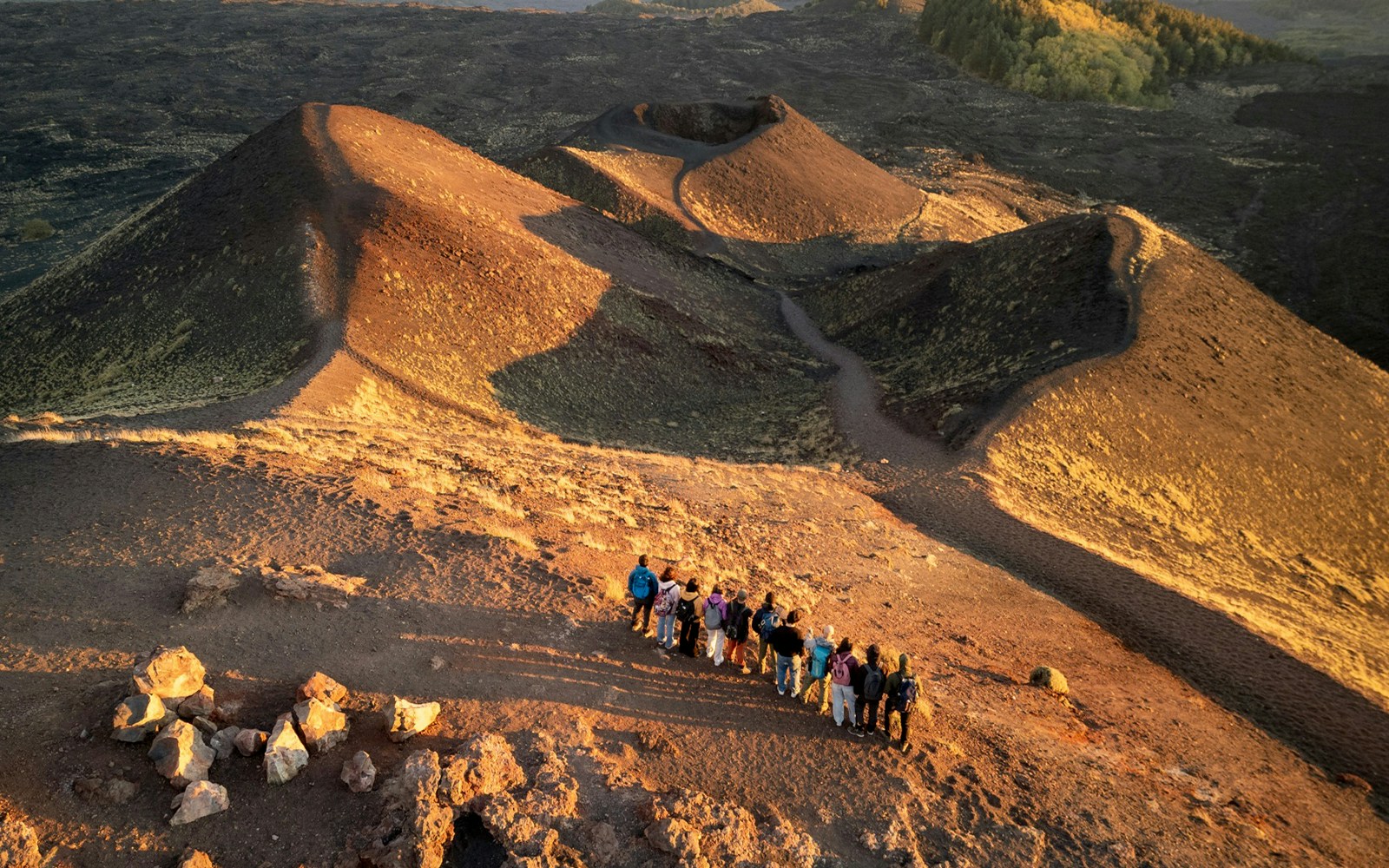 Tourists on Mount Etna at sunset, viewing volcanic craters and landscape.