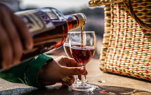 Pouring red wine into a glass beside a woven basket during a private electric tuk tuk tour.