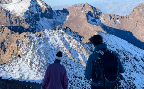 Two hikers overlooking snow-capped peaks during Mount Toubkal trek from Marrakech.