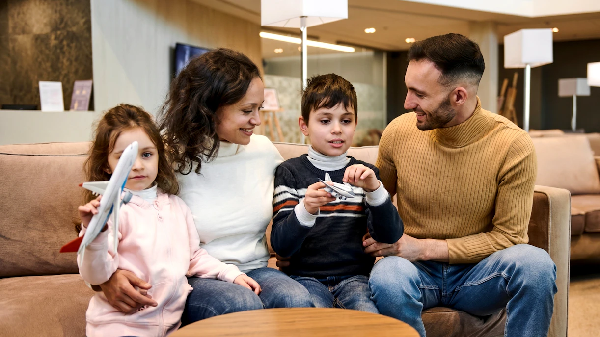 Family with children in airport VIP lounge holding toy airplanes.